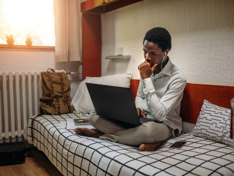 person sitting on bed with legs folded on laptop. (trending apps for college students)